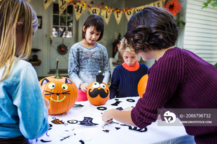 Mother assisting children in decorating pumpkins at table during Halloween party