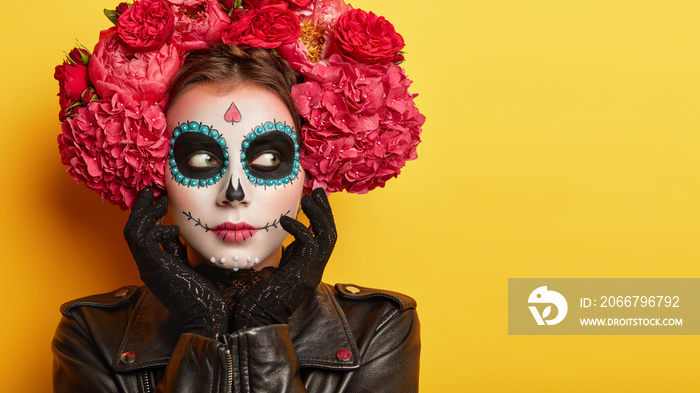 Horizontal shot of thoughtful female with Halloween creative makeup, looks away, has spooky look, we