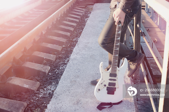 A man with an electric guitar on the railway. A musician in a leather jacket with a guitar on the street in the industrial zone.