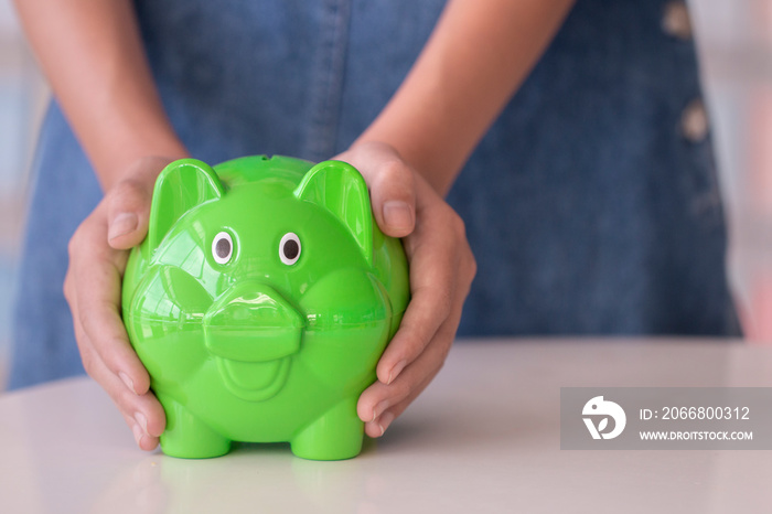 hand holding bright green piggy bank and money