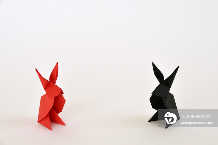 Red and black origami paper rabbits on white background.