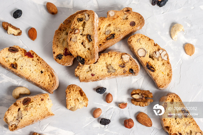 Tasty traditional Italian homemade biscotti or cantuccini cookies with hazelnuts, almonds, raisins and walnuts on a light gray background.