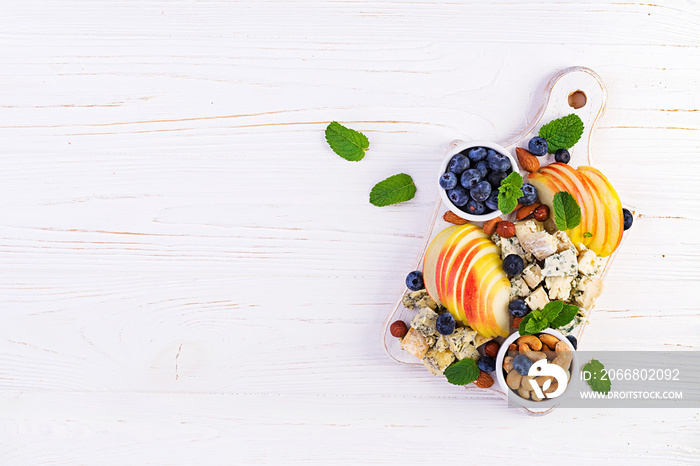 Cheese platter with assorted cheeses, blueberry, apples, nuts on white table. Italian cheese  platter and fruit. Top view, overhead