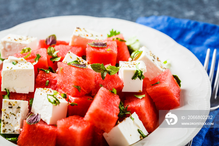 Watermelon salad with feta cheese and herbs in a white plate on blue background.