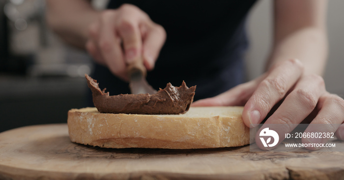 man spreading chocolate hazelnut spread on bread slice on wood board