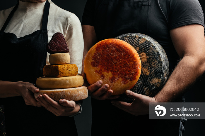 craftsmanship hands have a typical Italian cheese. French tomme cheese in the hands of a cheesemaker on dark background. Different homemade cheeses. Long banner format