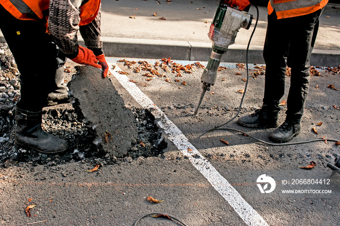 Workers remove a layer of old asphalt with a jackhammer on an autumn day.