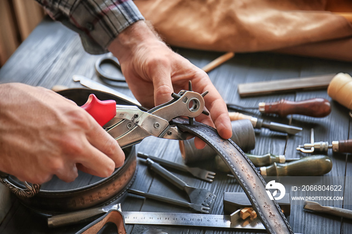 Man using leather punch while working with belt at factory, closeup