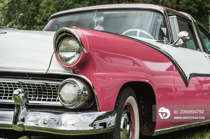 Partial front view of pink and white classic car from the fifties