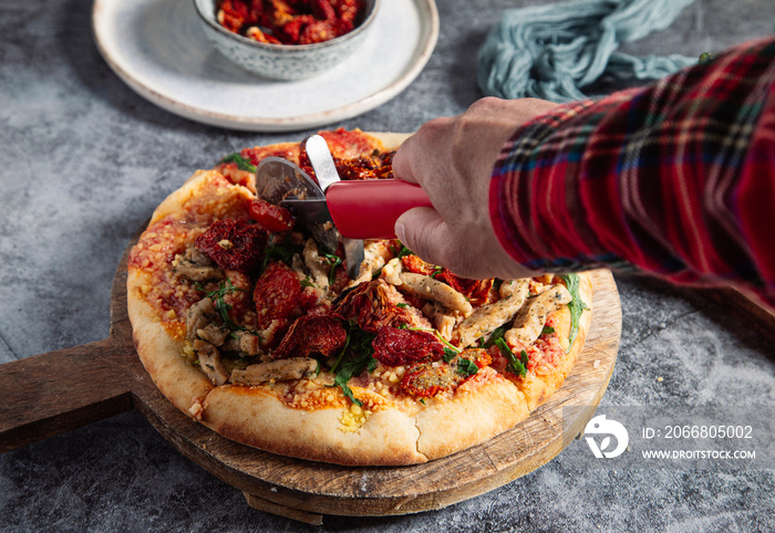 Man’s hand holds cutter over hot italian pizza on gray marble background.