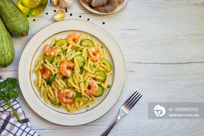 Italian Traditional Dish Trofie con Gamberi e Zucchine ,trofie pasta with prawns,zucchini,olive oil,garlics,parsley,salt and peppers on plate with white wood table background.Top view.Copy space