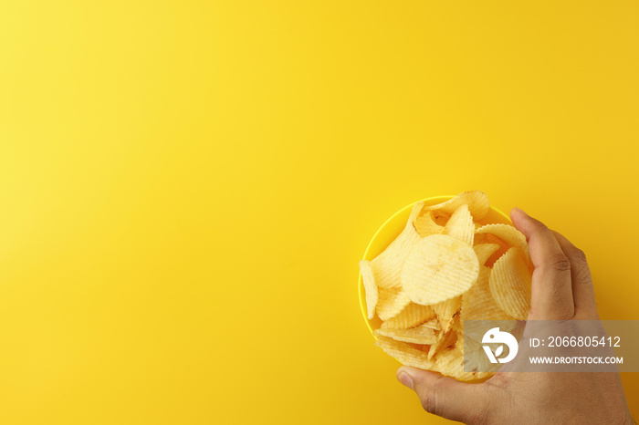 The man’s hand was holding a yellow bowl with crispy potato chips inside the bowl fast food has a salty taste. Has energy, calories, energy, high carbohydrate. Image top view flat lay with copy space.