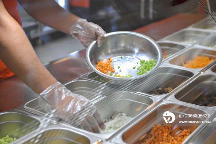 the cook puts pieces of vegetables for salad in a bowl. tray with assorted for salad in the window of a fast food restaurant