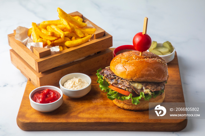 Homemade hamburger served with french fries. It looks delicious prepared with onions, hamburger patties, cheddar cheese and ham.