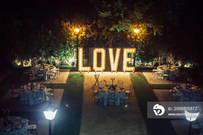 tables prepared for the banquet of a wedding in a garden with a luminous giant letters