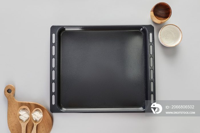 Baking tray with bowls, spoon of flour and board on light background