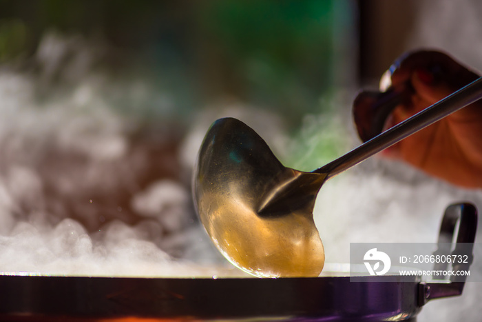 Cooking person in the restaurant is cooking while using the dipper in a large pot. And the water is boiling, there is smoke, hot spit.