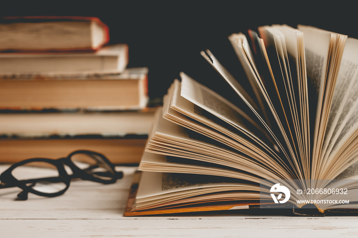 An open book with glasses on a wooden table against the background of a set of books, vintage toning. Literature, learning concept