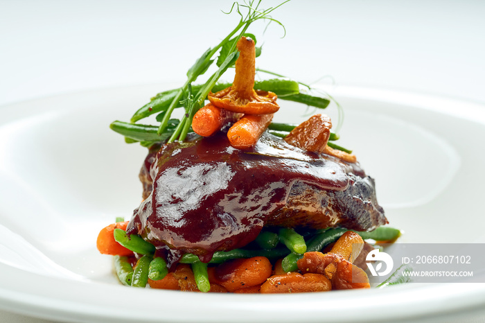 Beef cheek steak, caramelized in wine sauce with chanterelles and asparagus in a white plate. Isolated on grey background.