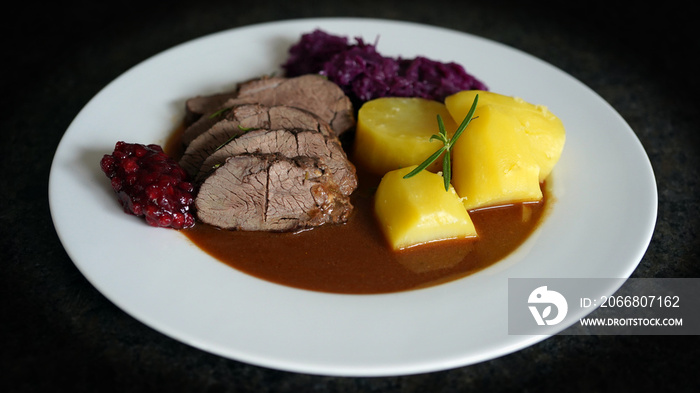 delicious meal from a young chamois buck with potatoes and red cabbage, brown sauce and cranberries on a white plate