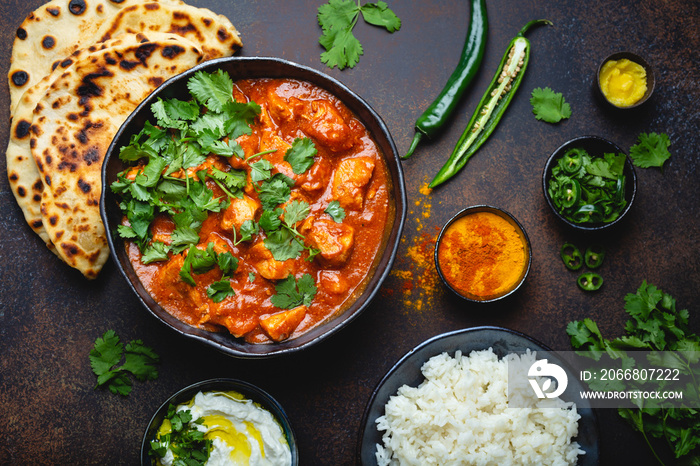 Traditional Indian dish Chicken tikka masala with spicy curry meat in bowl, basmati rice, bread naan, yoghurt raita sauce on rustic dark background, top view, close up. Indian style dinner from above