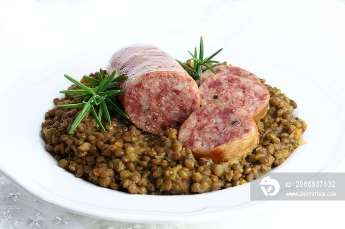 Cotechino con lenticchie servito su un piatto isolato su sfondo bianco. Decorazioni natalizie. Cibo italiano.