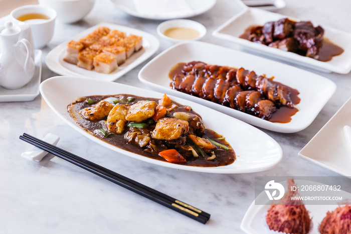 Deep fried snapper fillets stir fried with black pepper, onion, bell pepper, carrot and XO sauce with BBQ Pork and Crispy Pork Belly in background.