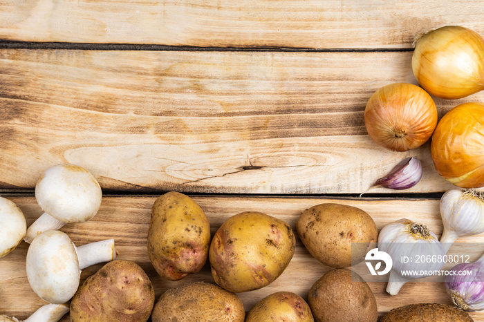 Potatoes, mushrooms, onions and garlic on a wooden background.