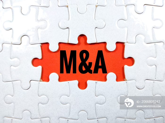 Selective focus.Word M and A (mergers and acquisitions) with jigsaw puzzle on red background.Business concept.