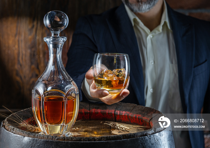 Whisky tasting. Man sits in front of a barrel with a decanter and a glass of whiskey.