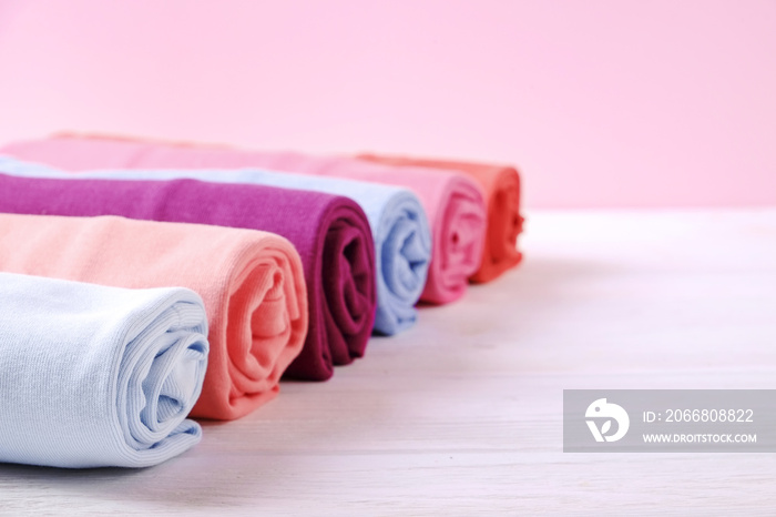 Close up of colorful clothes neatly rolled for saving luggage space, stack of cotton t-shirt rolls of different pastel colors on wooden texture table. Background, close up, copy space, top view.