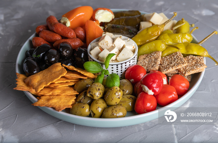 Plate with various party snacks and antipasti on a gray background.