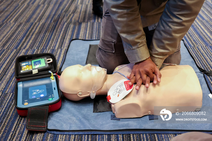 Asian man practicing CPR on a plastic mannequin with Automated External Defibrillator (AED) on the floor.