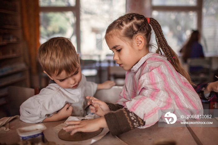 Cute little kids playing together with modeling clay in pottery workshop, craft and clay art