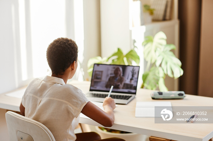 Back view portrait of African American girl watching online lesson while studying at home in sunlight, copy space