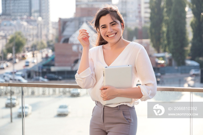 Beautiful brunette business woman in white skirt and grey suit trousers working on a tablet in her hands outdoors. European city on background. copy space