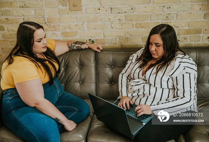 2 plus size women sit and work on sofa