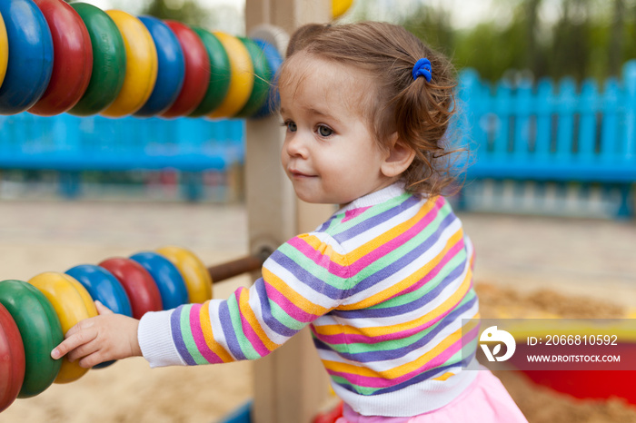 a little girl with two tails is dressed in a striped colorful jacket is playing in the sandbox on the playground