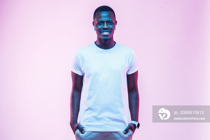 Attractive young african man posing in blank white cotton t-shirt, standing isolated on pink background