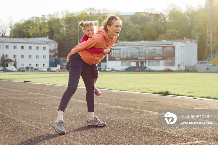 Sports cheerful family, healthy lifestyle, spring portrait of mother and little daughter having fun and running at the stadium