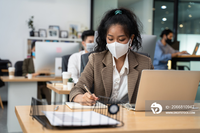 Asian young businesswoman wearing mask, working on computer in office.