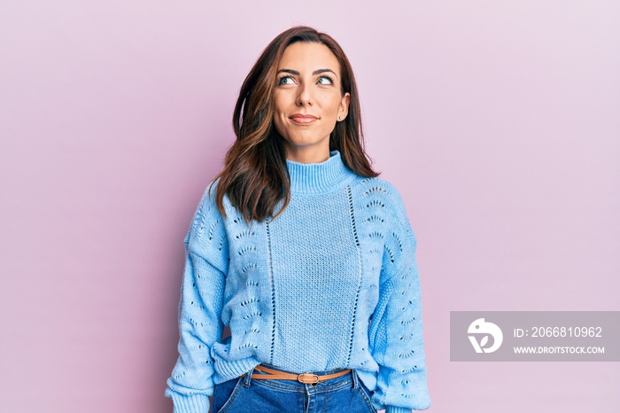 Young brunette woman wearing casual winter sweater over pink background smiling looking to the side and staring away thinking.