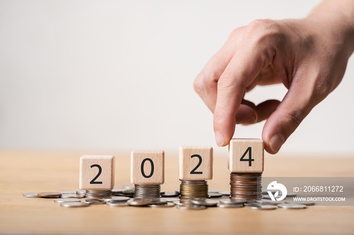 2024 new year goals planning concept, wooden cubes on stack of coins, positive indicator 2024, investment finance planning for the new year 2024.