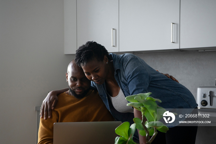 Man and pregnant woman looking at laptop in kitchen