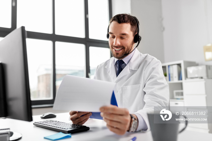 healthcare, medicine and technology concept - happy smiling male doctor with headset, computer and clipboard working at hospital