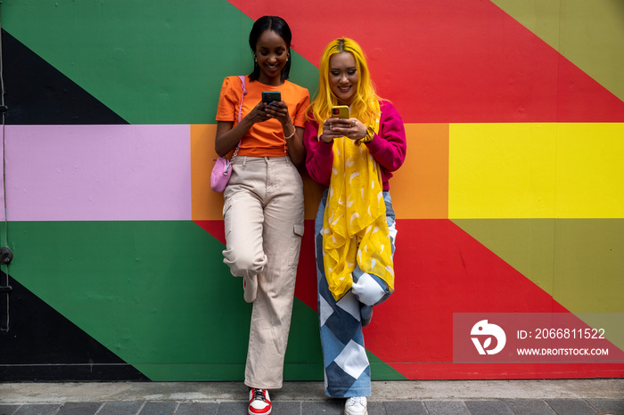 Young female friends using phones outdoors