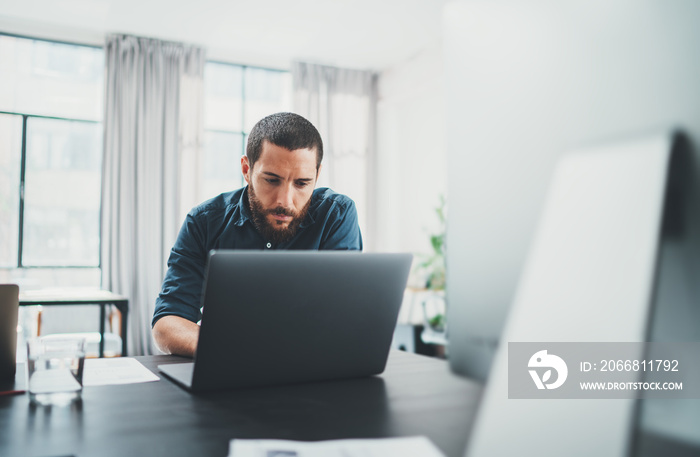 Young coworker working at lightful office on computer while sitting at the wooden table