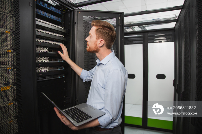 Processing system. Focused IT technician examining server closet while holding laptop