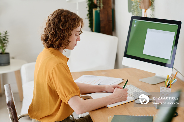 Side view of young businesswoman or freelancer in casualwear working in front of computer screen with small blank window