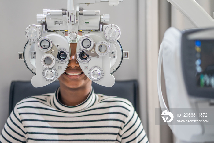 Close-up Of african teen girl Doing Eye Test On Phoropter, African teen girl checking on her eye with optometry machine.